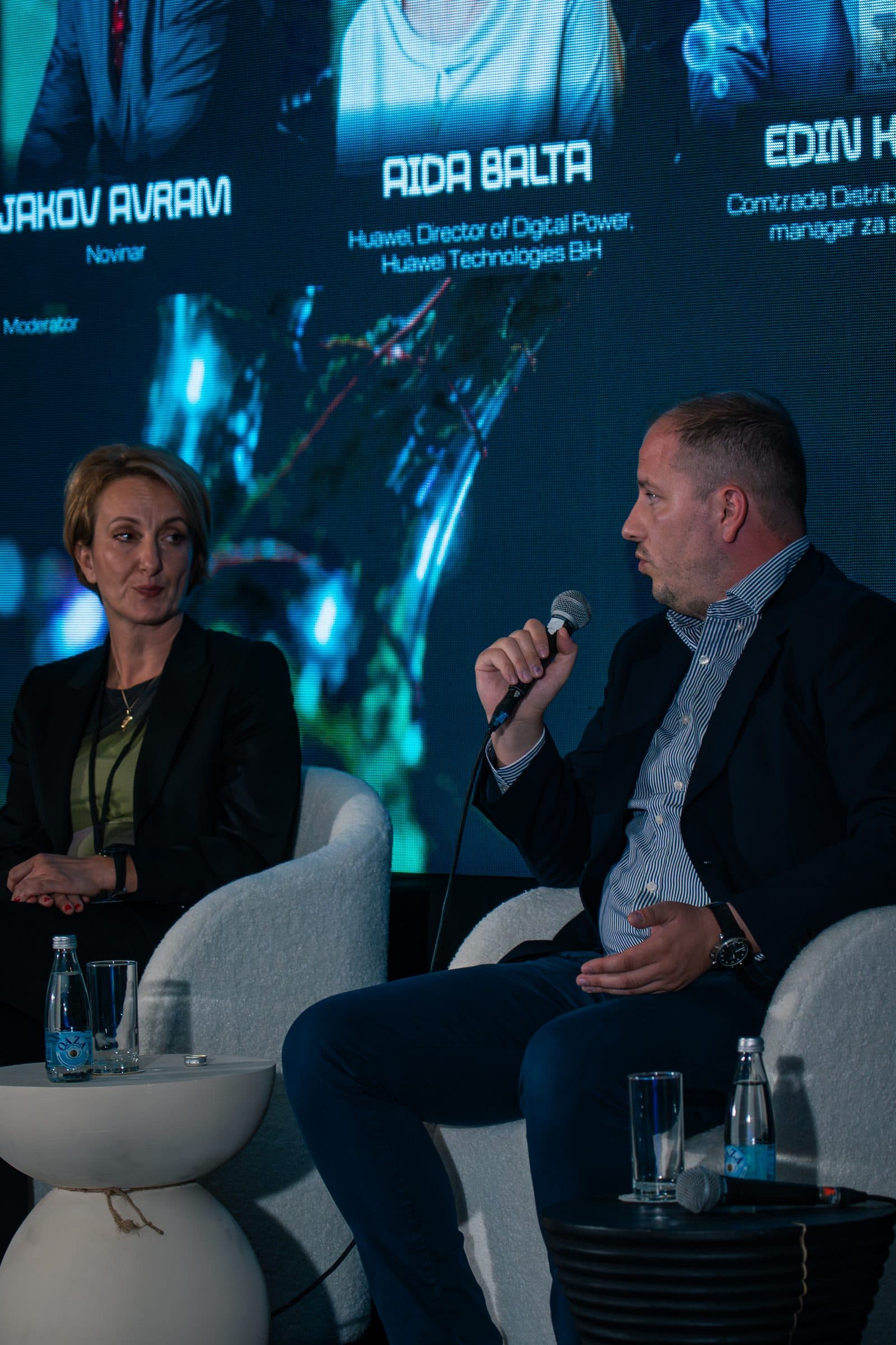 Panelista govori u mikrofon dok ga panelistkinja pored njega sluša, iza njih LED ekran