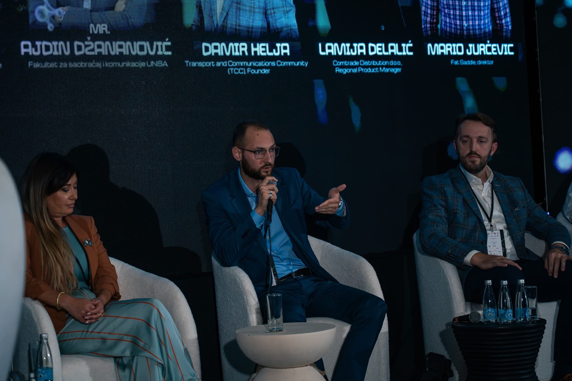 Panelista objašnjava s mikrofonom u ruci, iza njega imena govornika na ekranu