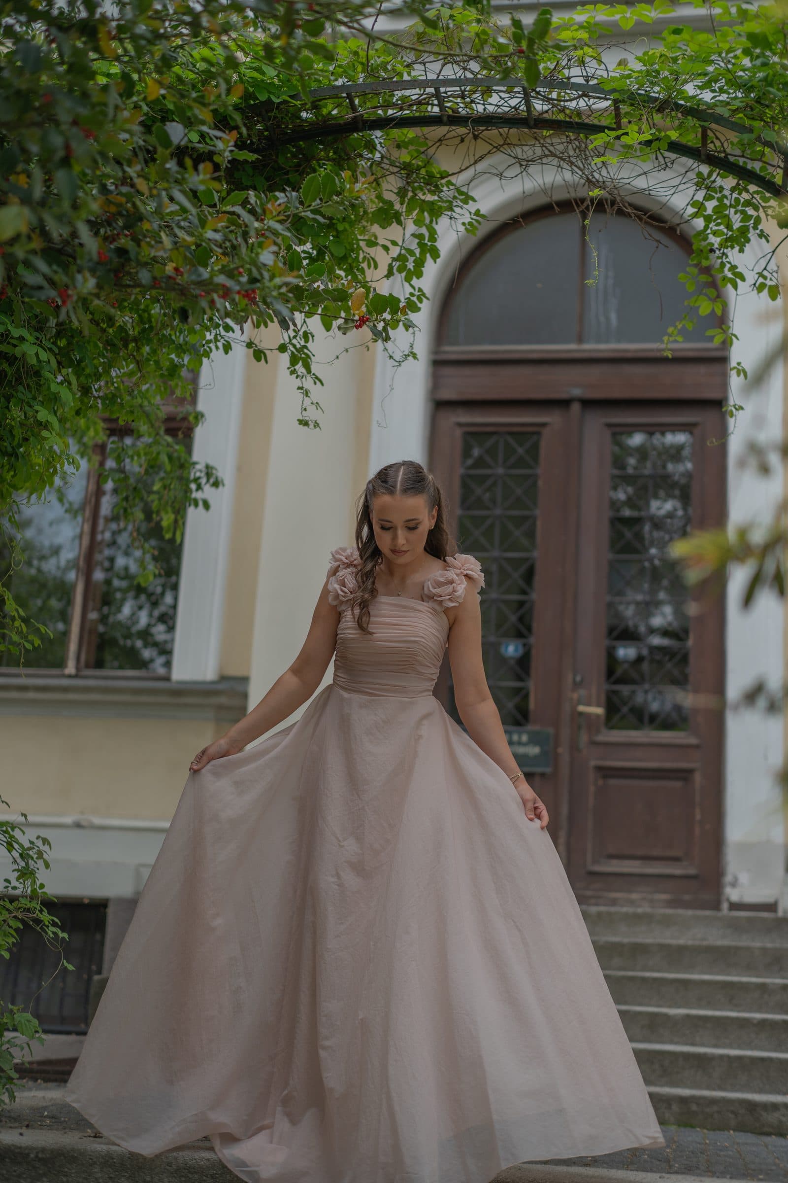 Sumeja spreading her gown under a leafy arch in front of an old wooden door