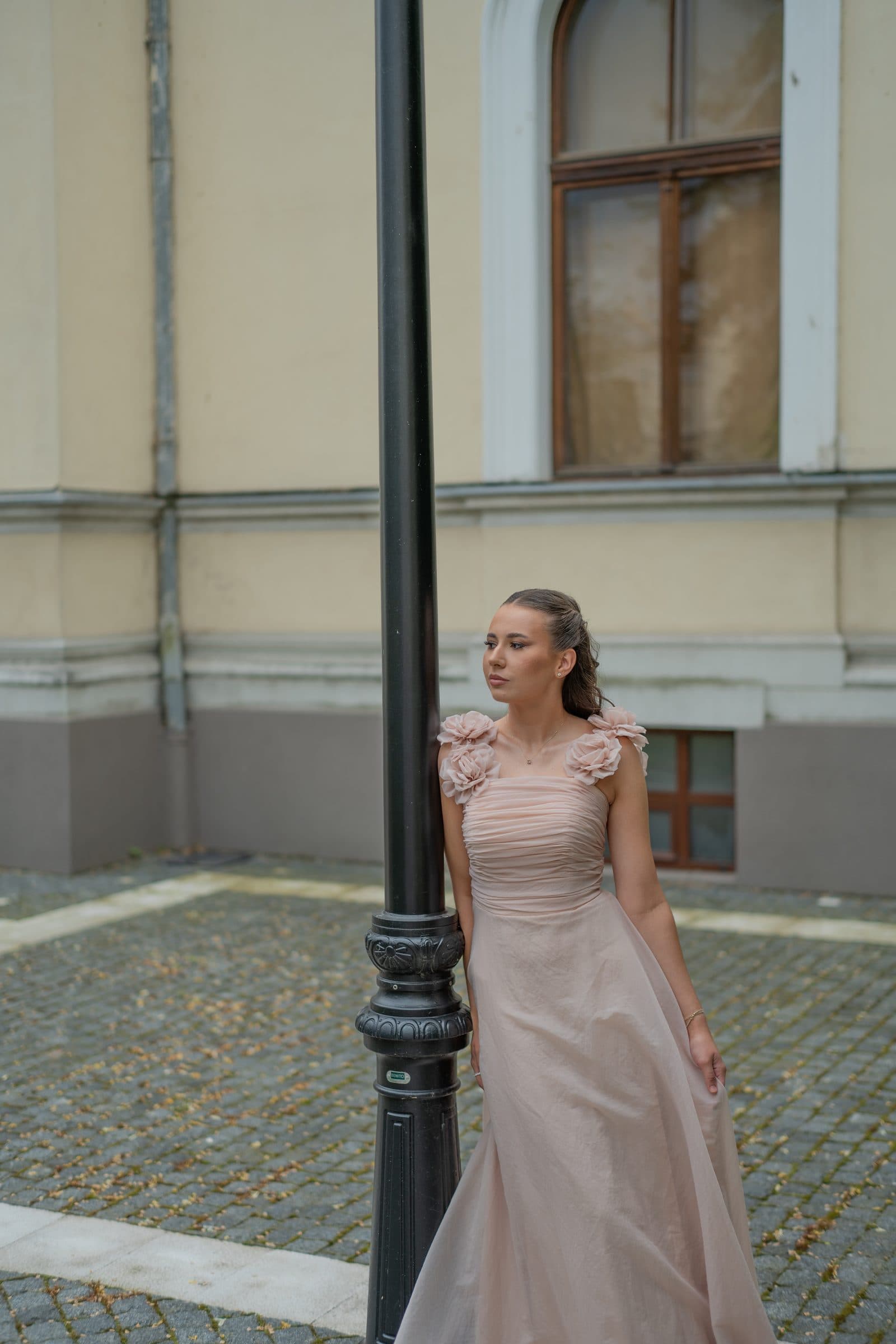 Sumeja leaning on a street lamp in a cobbled courtyard