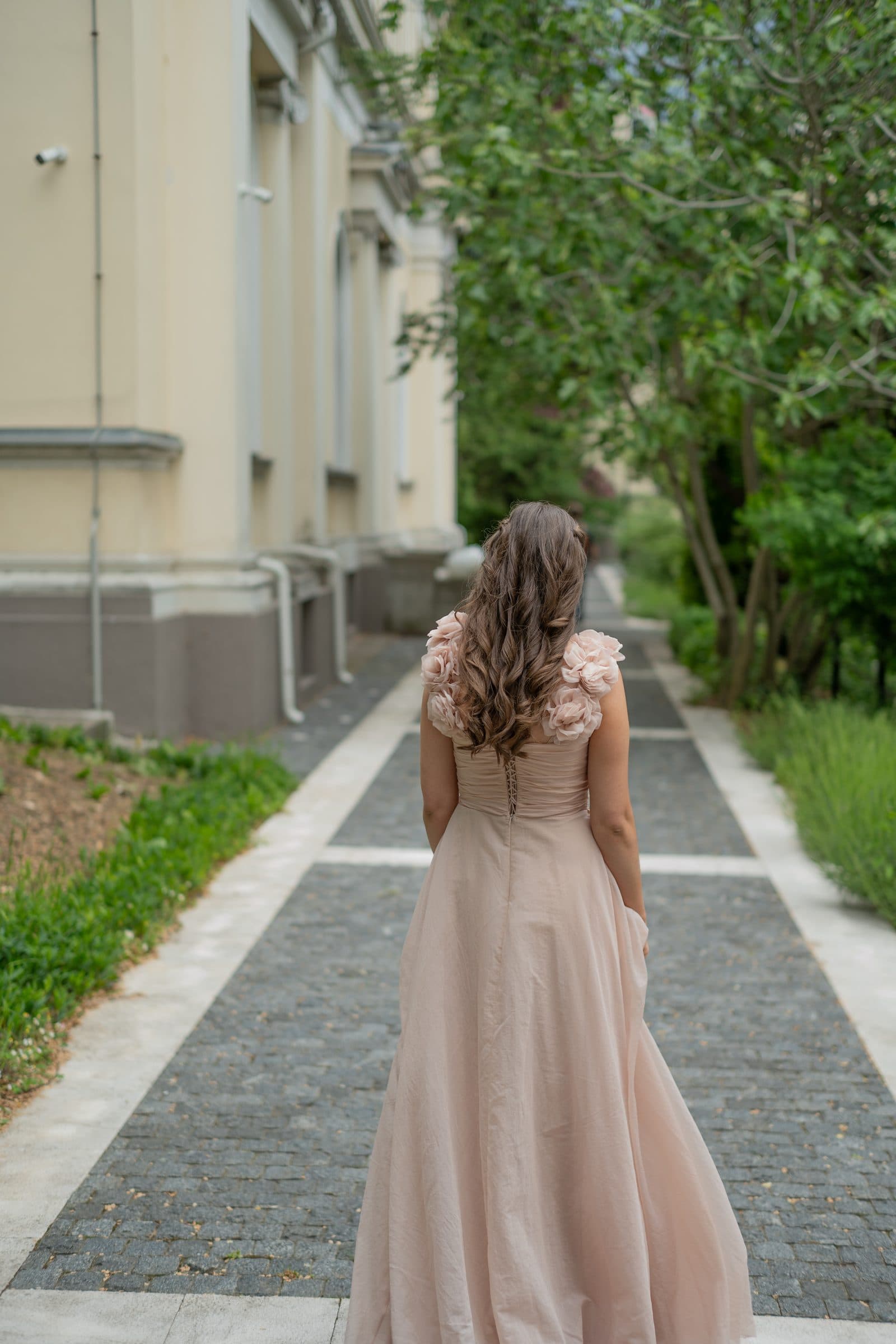 Sumeja from behind on a stone path, with long curls and rose straps