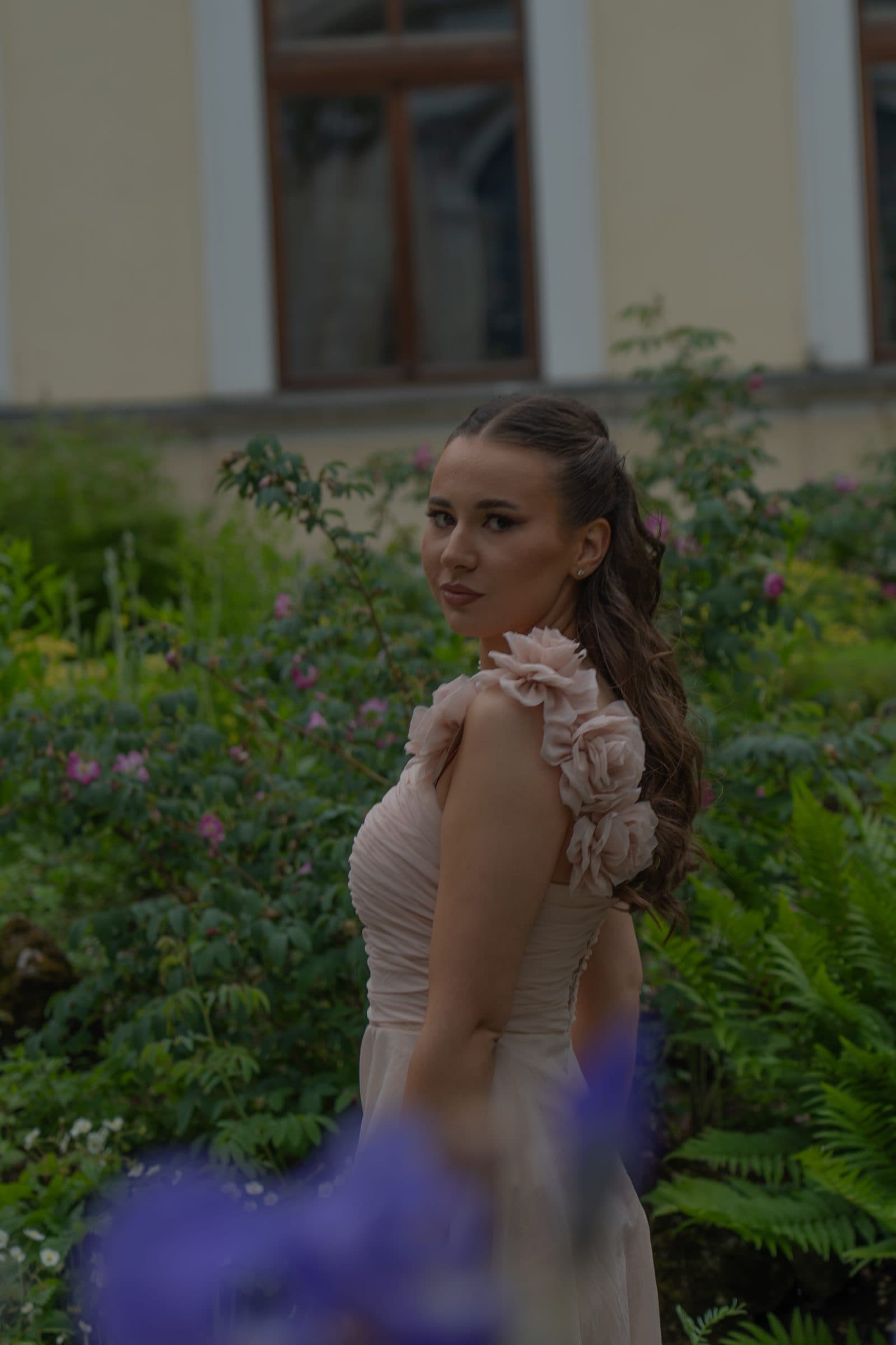 Sumeja looking over her shoulder in a garden, purple flowers in the foreground