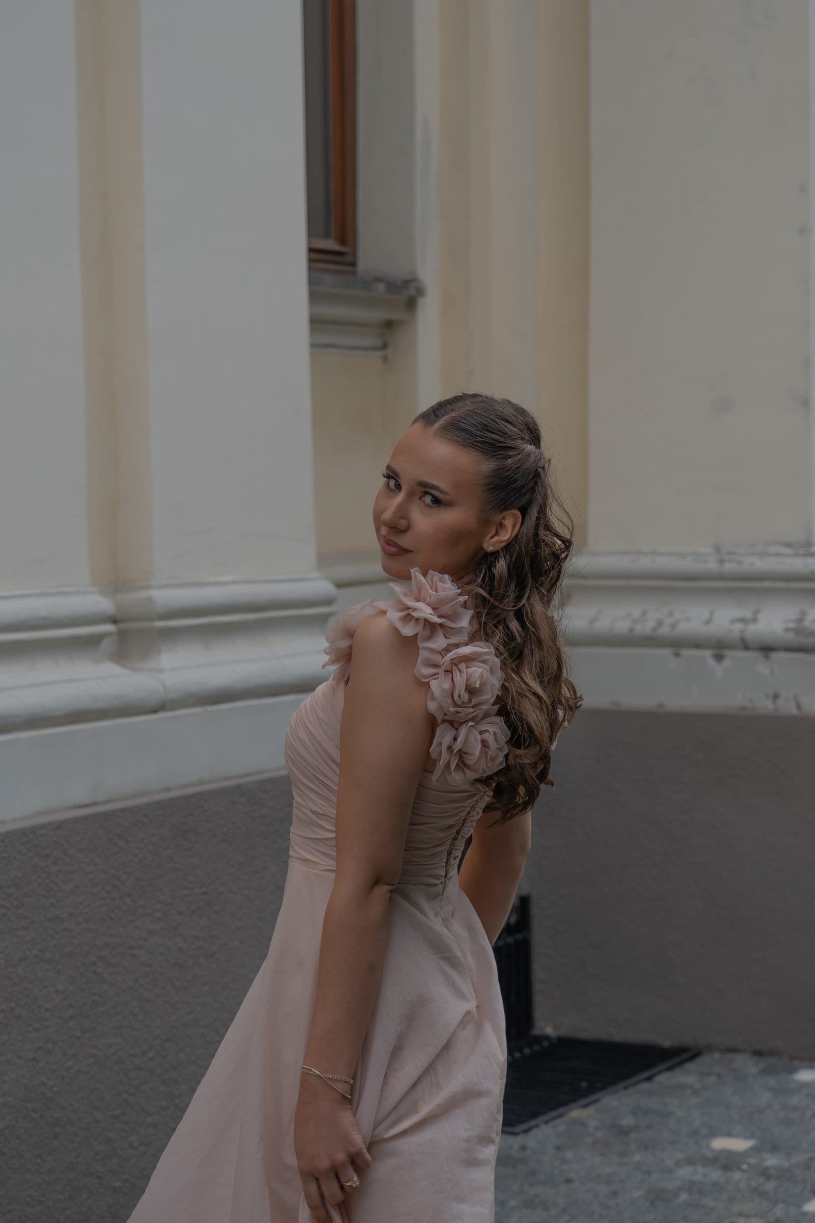Sumeja glancing back over her shoulder by a pale building