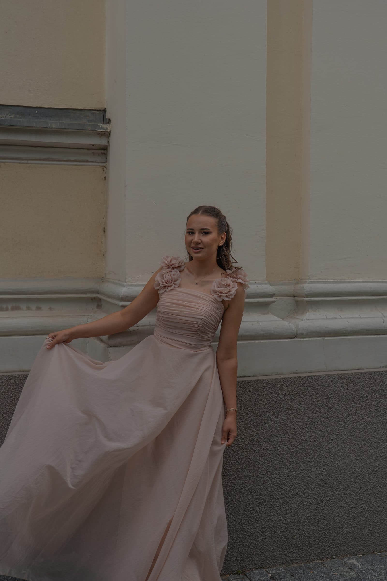 Sumeja holding out her gown against a pale wall